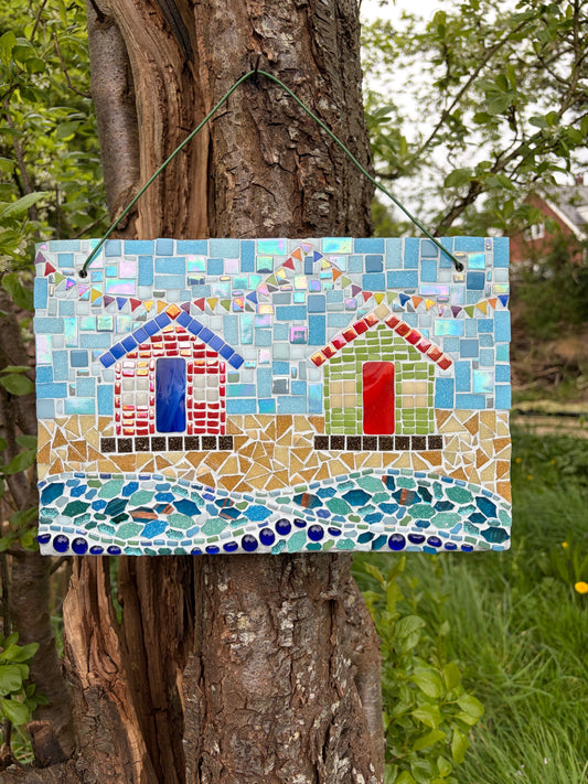 Handcrafted mosaic beach hut art on slate with twin huts, colourful bunting and crashing wave detail, hung on a tree