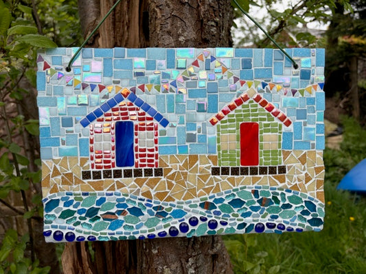 Close-up of mosaic beach hut art showing red-brick and sage green huts with bunting and iridescent sky tiles