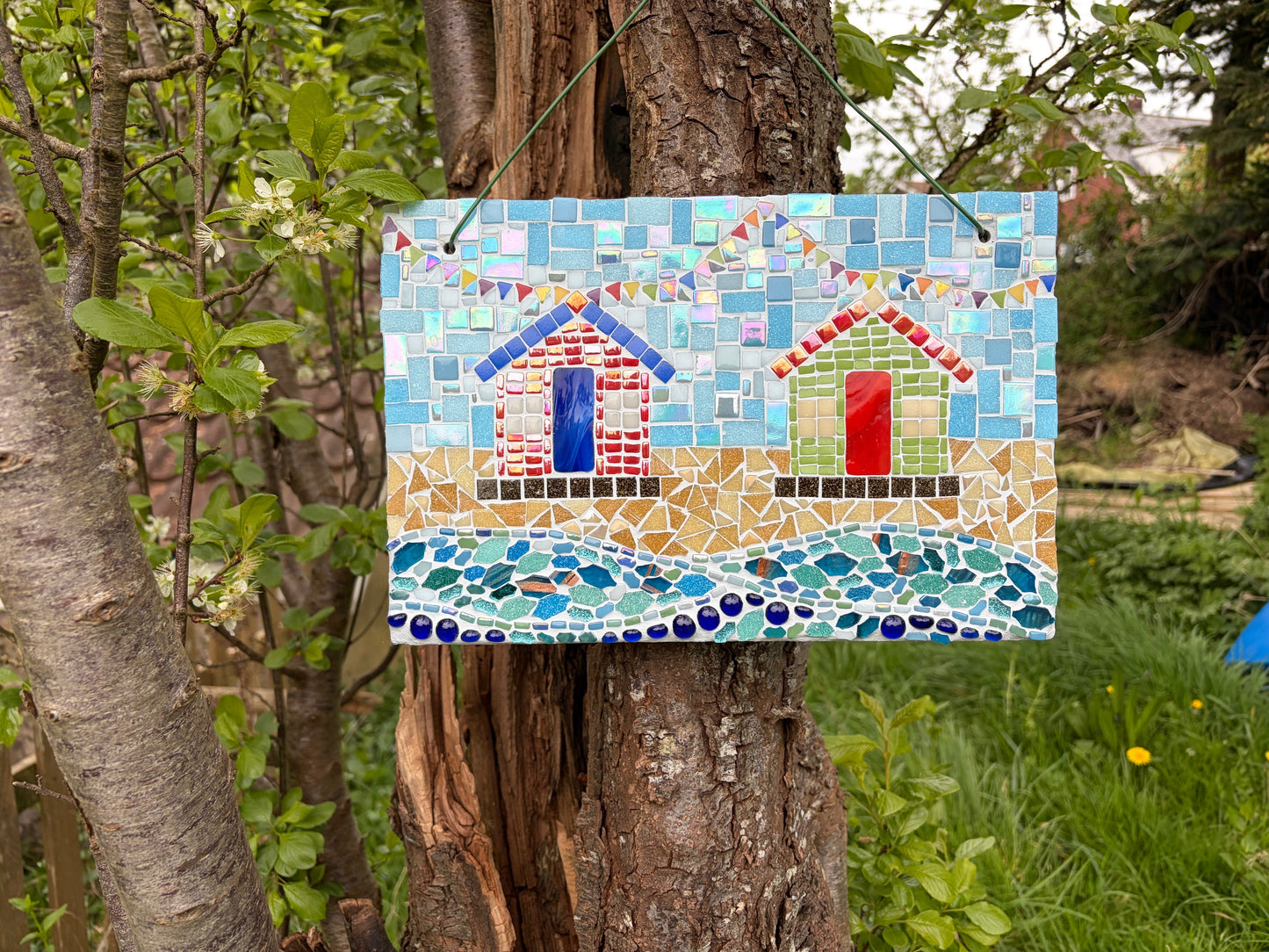 Mosaic beach hut garden art hung on a tree showing sandy shore and wave sections in detail