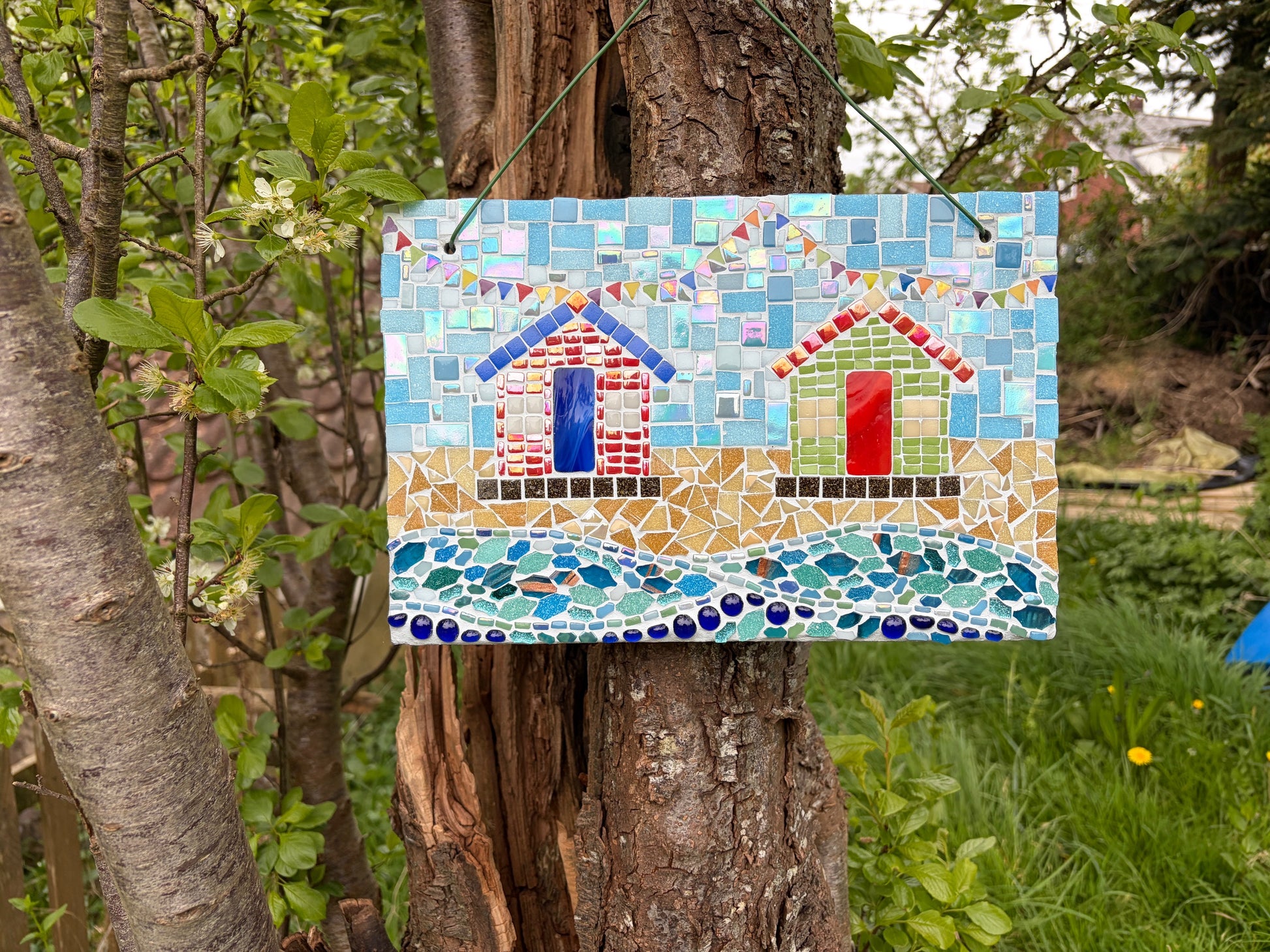 Mosaic beach hut garden art hung on a tree showing sandy shore and wave sections in detail