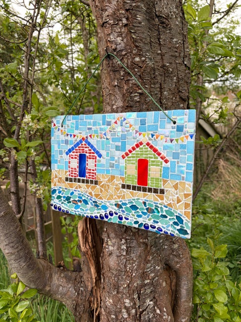 Mosaic beach hut slate art photographed from a distance showing full scene with bunting, huts and waves