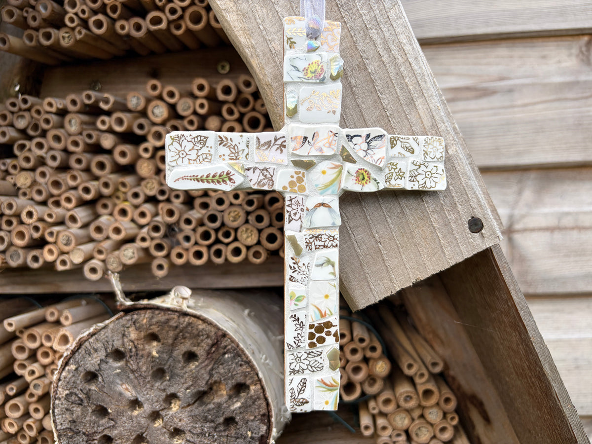 Handcrafted mosaic cross made from vintage botanical china fragments in soft whites and creams with iridescent glass centre and white ribbon loop