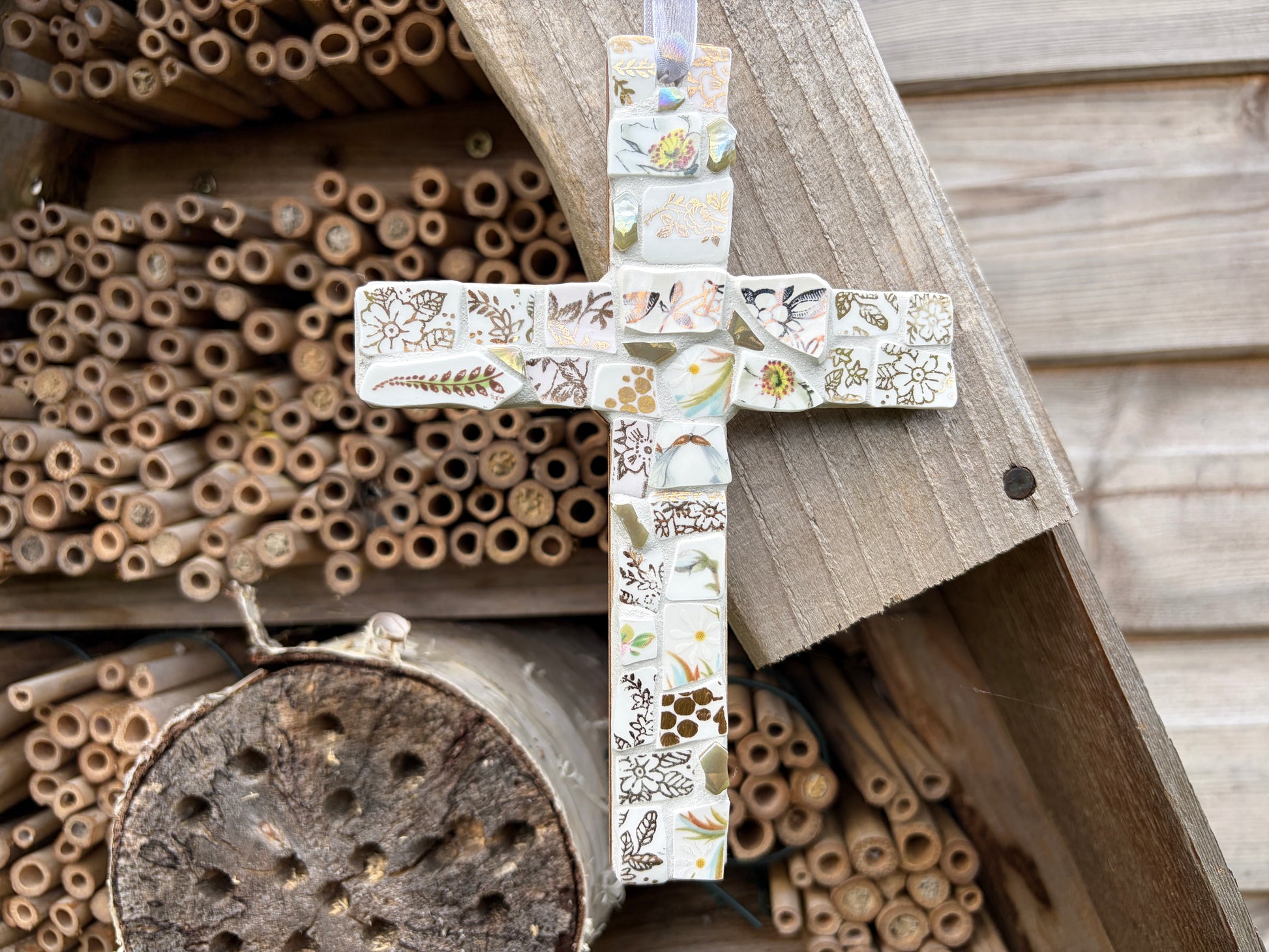 Handcrafted mosaic cross made from vintage botanical china fragments in soft whites and creams with iridescent glass centre and white ribbon loop
