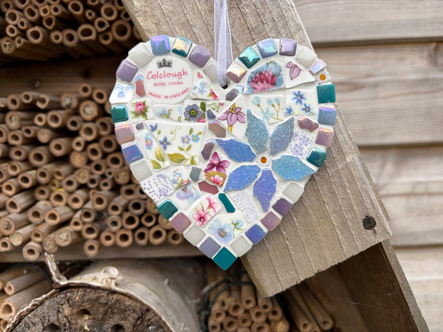 Handcrafted mosaic heart hanging made from vintage Colclough bone china with pink and blue florals, teal and lilac tile border, iridescent blue centrepiece and white ribbon loop