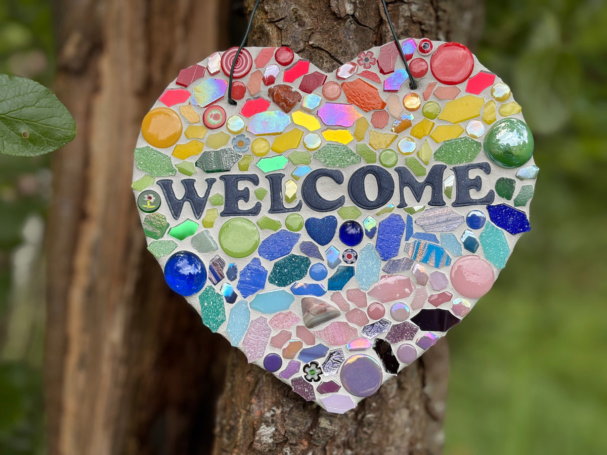 Rainbow mosaic heart welcome sign on slate with glass gems and iridescent tiles hung on a tree, close-up