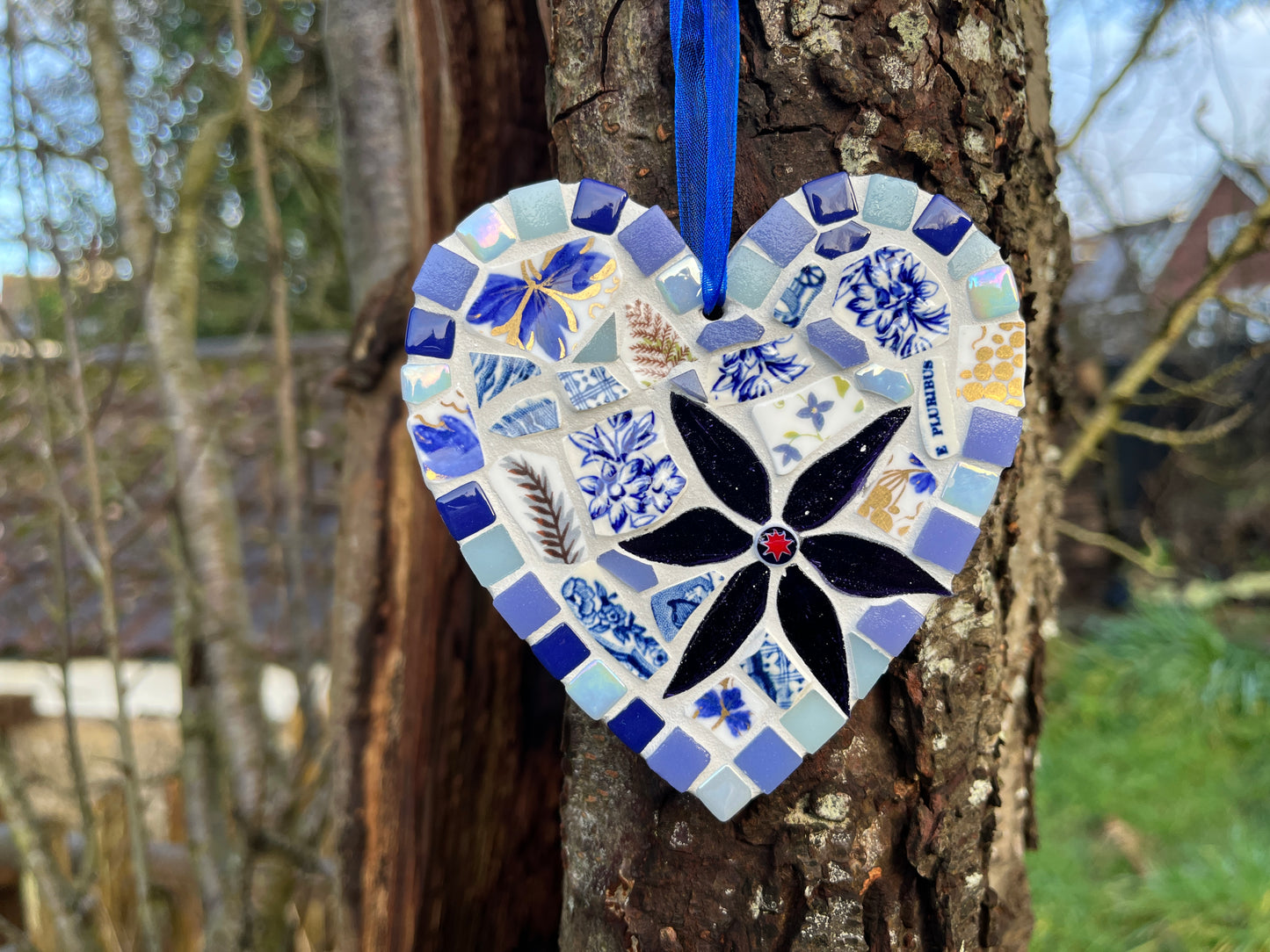Handcrafted mosaic heart using vintage blue and white floral china with cobalt and iridescent tile border and midnight black glass flower with red star centre, hung on a tree