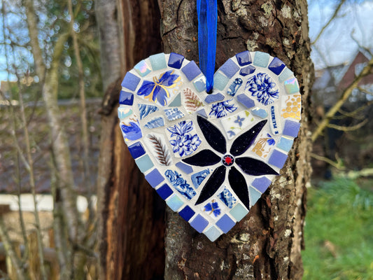 Handcrafted mosaic heart using vintage blue and white floral china with cobalt and iridescent tile border and midnight black glass flower with red star centre, hung on a tree