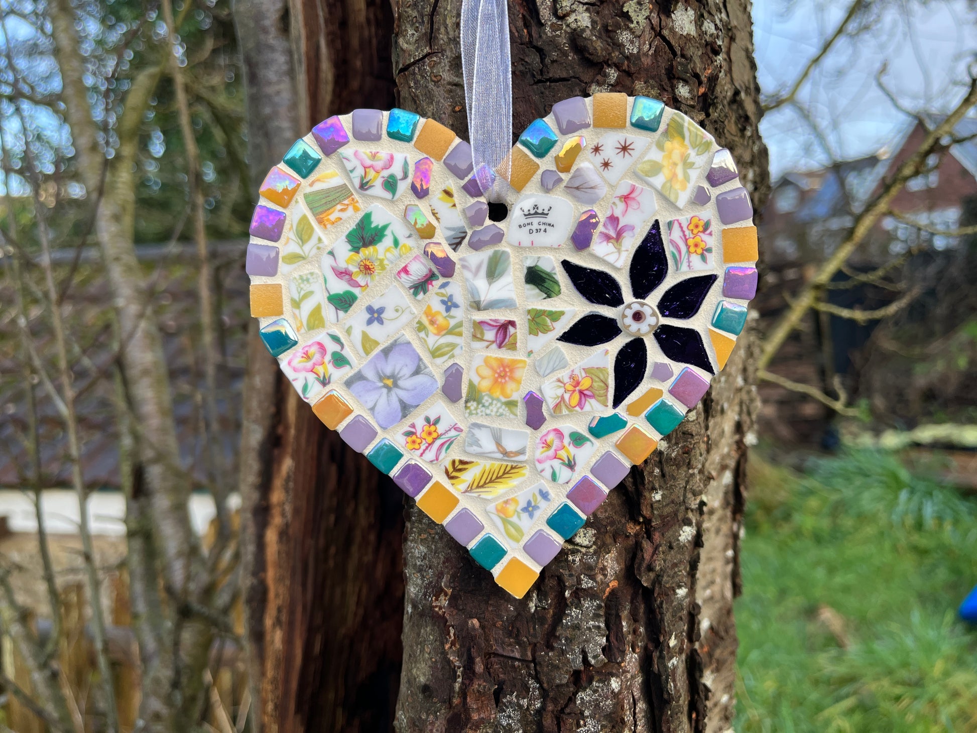 Handcrafted mosaic heart using vintage wildflower bone china with amber yellow, lavender and teal tile border and black glass flower centrepiece, hung on a tree