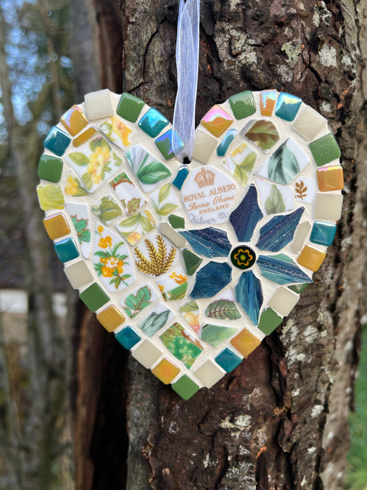 Handcrafted mosaic heart using Royal Albert Silver Maple bone china with teal, amber and sage green tile border and blue glass flower centrepiece, hung on a tree