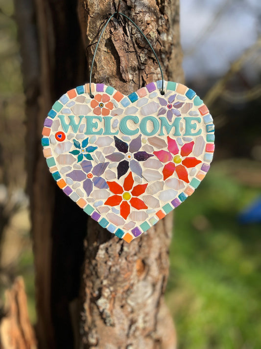 Handcrafted mosaic floral welcome heart on slate with teal ceramic WELCOME lettering, colourful flower mosaic and rainbow tile border, hung on a tree
