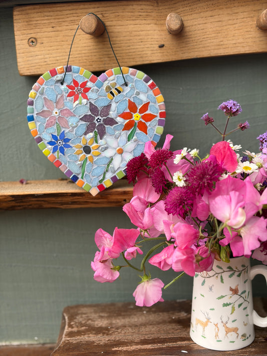 Rainbow floral mosaic heart hung on a wooden peg rack alongside a jug of fresh flowers